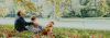 A father, his son, and their dog sitting under a tree looking away from the viewer.